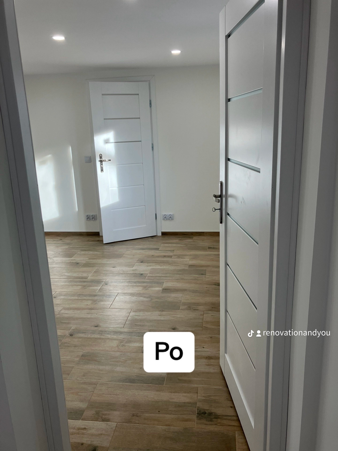 Wykończone wnętrze z drewnopodobną podłogą, białe ściany i dwoje białych drzwi z poziomymi frezowaniami, widok zza otwartych drzwi.