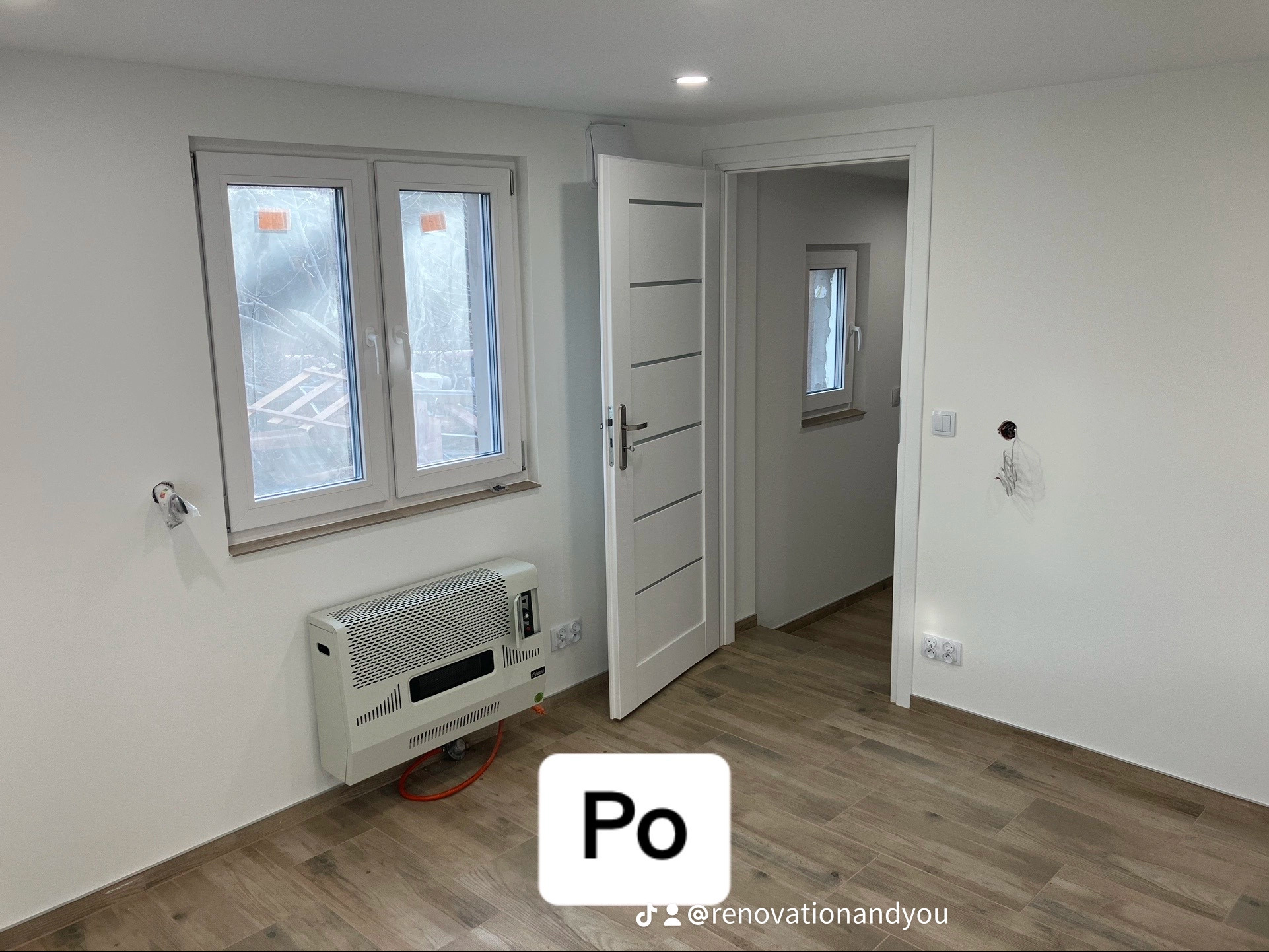 Wnętrze po remoncie: drewnopodobne panele, białe ściany, biała stolarka drzwiowa i okienna, grzejnik gazowy na ścianie, widoczne gniazdka elektryczne i wyprowadzone przewody.