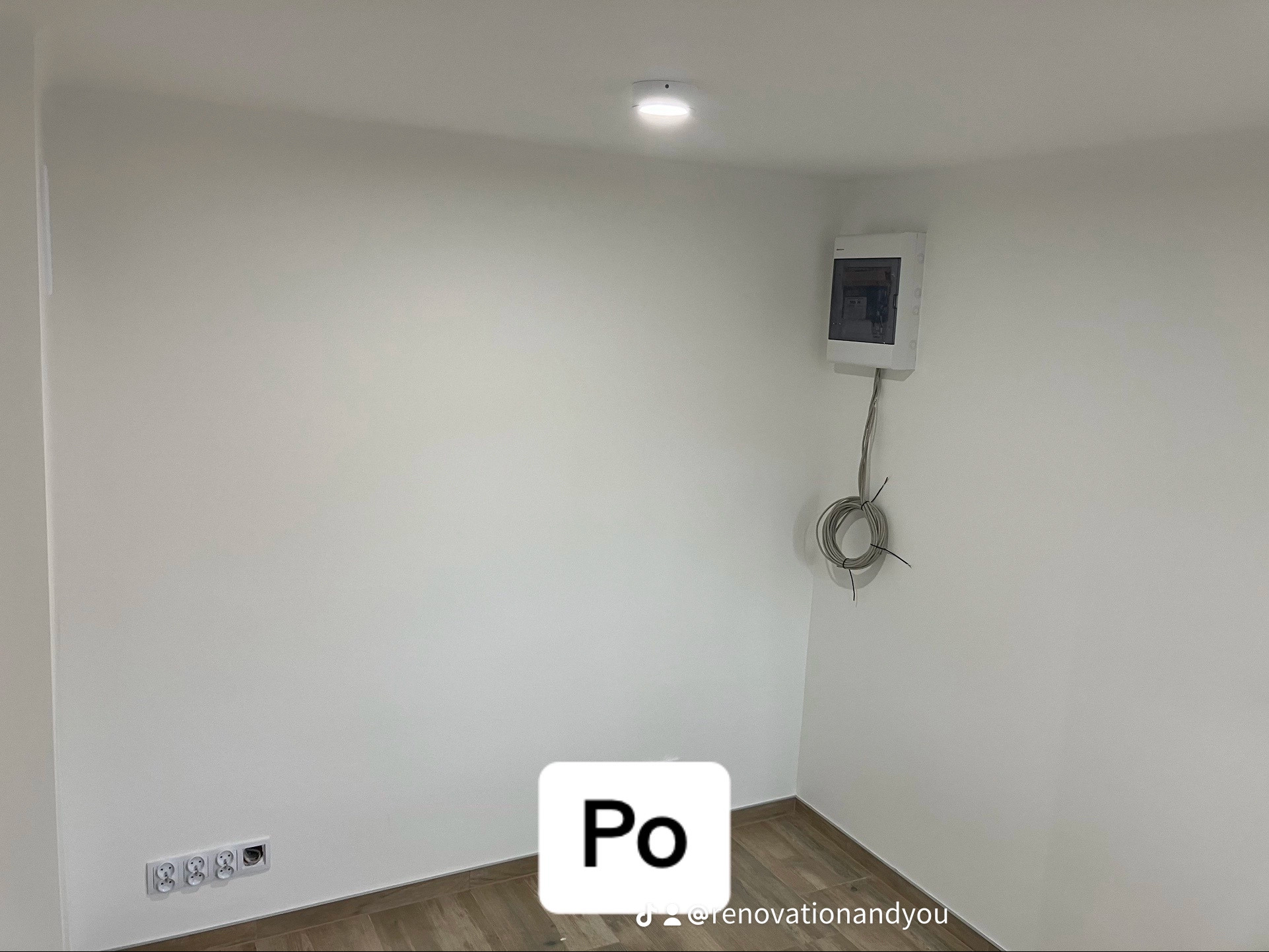 Wnętrze pokoju po remoncie: gładkie, białe ściany, drewnopodobne panele podłogowe, zamontowana skrzynka elektryczna z wystającymi kablami, gniazdka elektryczne.