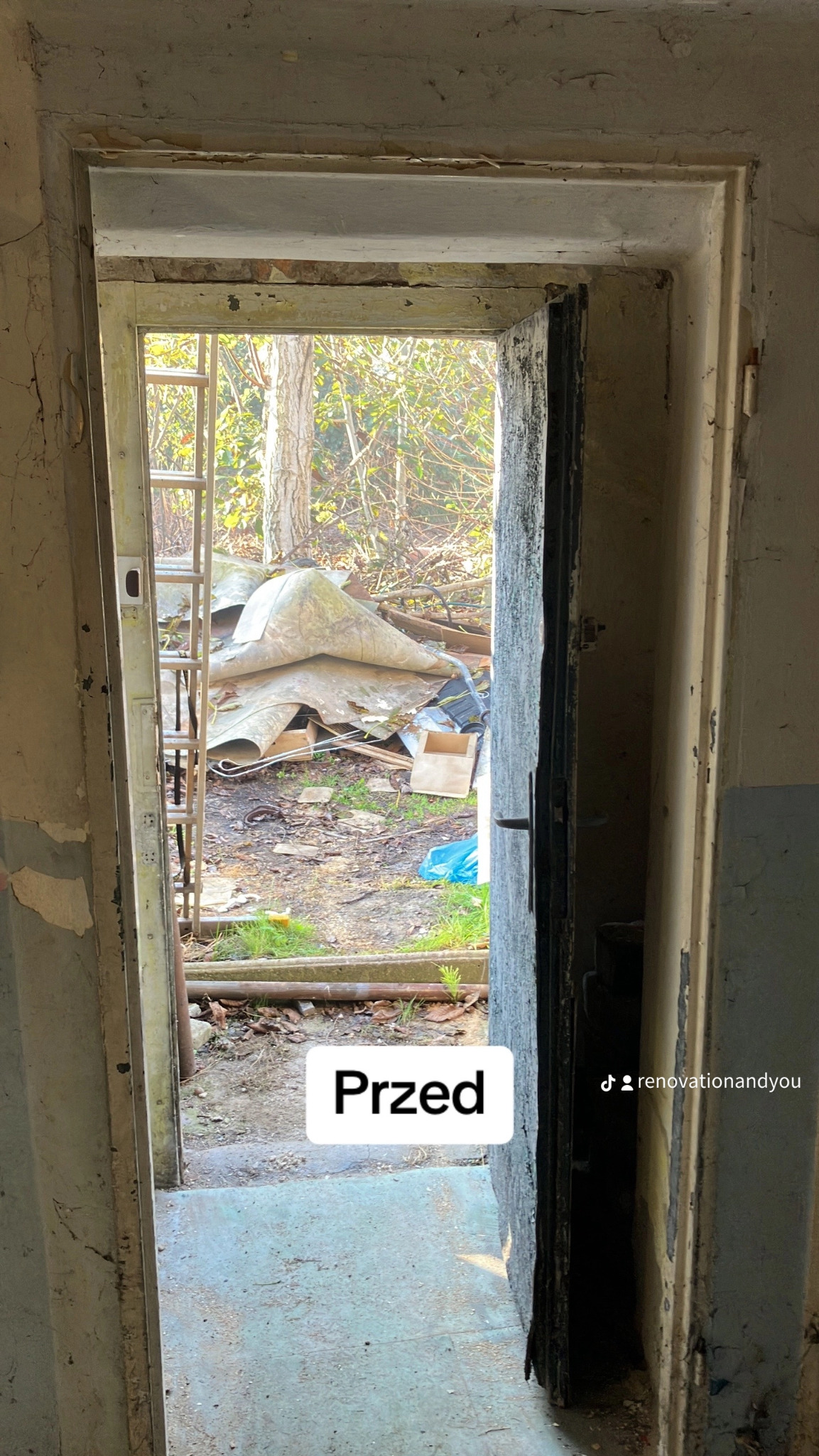 Zniszczone wejście do pomieszczenia przed remontem, widoczne odpadające fragmenty farby, stara stolarka drzwiowa i bałagan na zewnątrz.