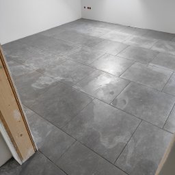 Zakład ogólnobudowlany Jacek oleszczuk - Szare, matowe płytki podłogowe ułożone w nowym pomieszczeniu z oknem dachowym, widoczne ślady po czyszczeniu na powierzchni płytek.