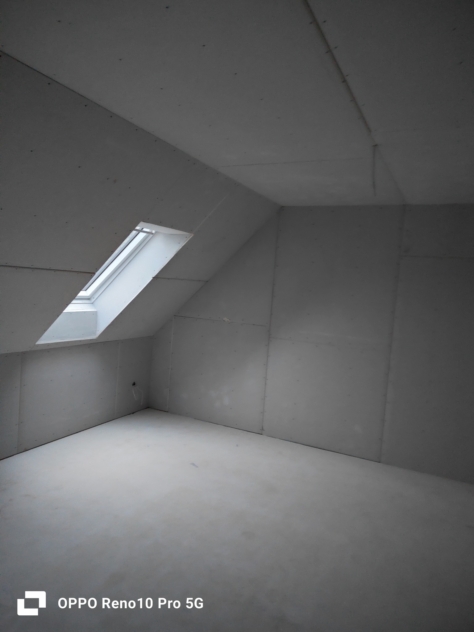 Poddasze z oknem dachowym, ściany wyłożone płytami gipsowo-kartonowymi, widoczne łączenia płyt.