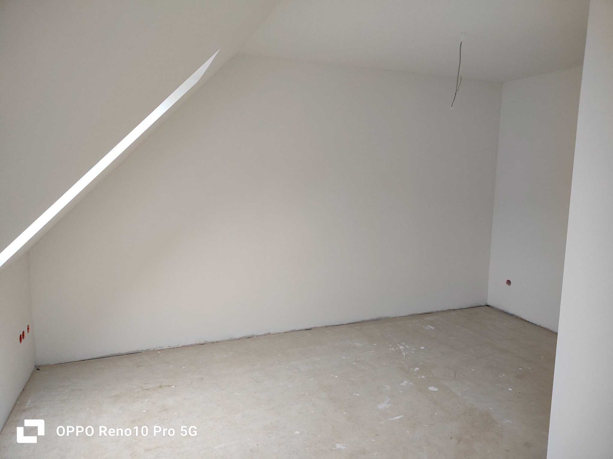 Pomalowane na biało poddasze ze skosem i wystającymi przewodami elektrycznymi, przygotowane do dalszych prac wykończeniowych.