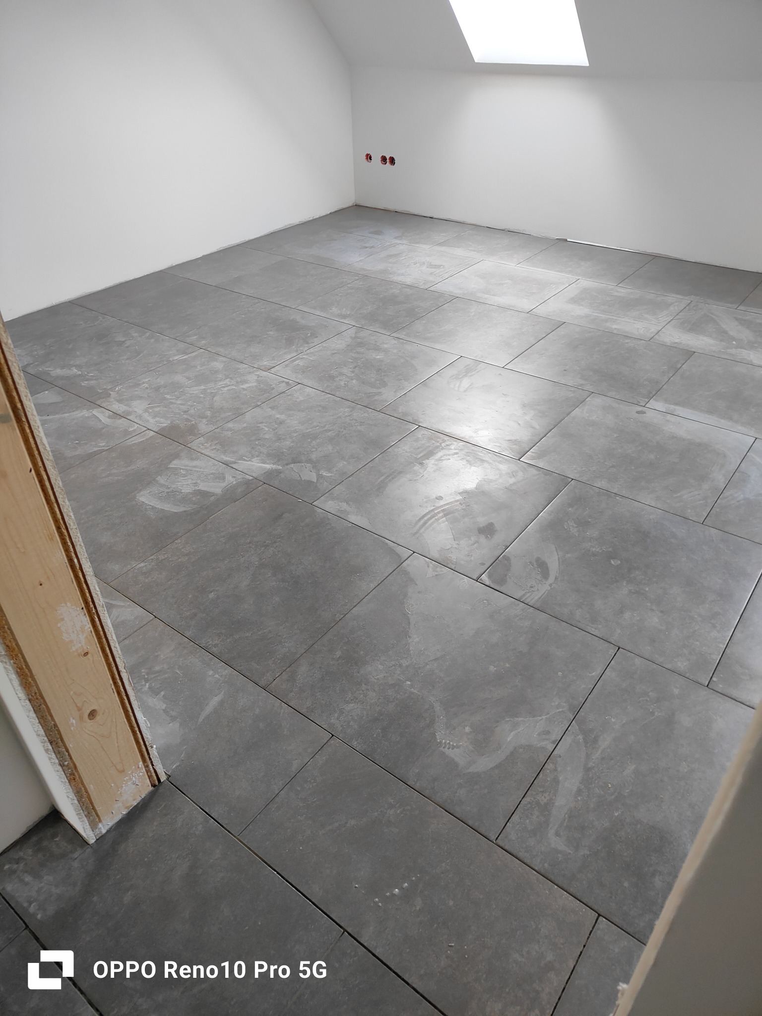 Szare, matowe płytki podłogowe ułożone w nowym pomieszczeniu z oknem dachowym, widoczne ślady po czyszczeniu na powierzchni płytek.