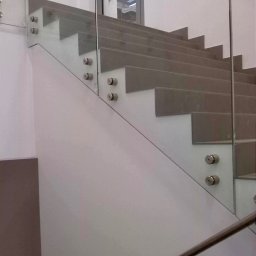 Studio Szkła Rzeszów - Schody z szarego kamienia zabezpieczone szklaną balustradą mocowaną punktowo, widoczne metalowe poręcze.