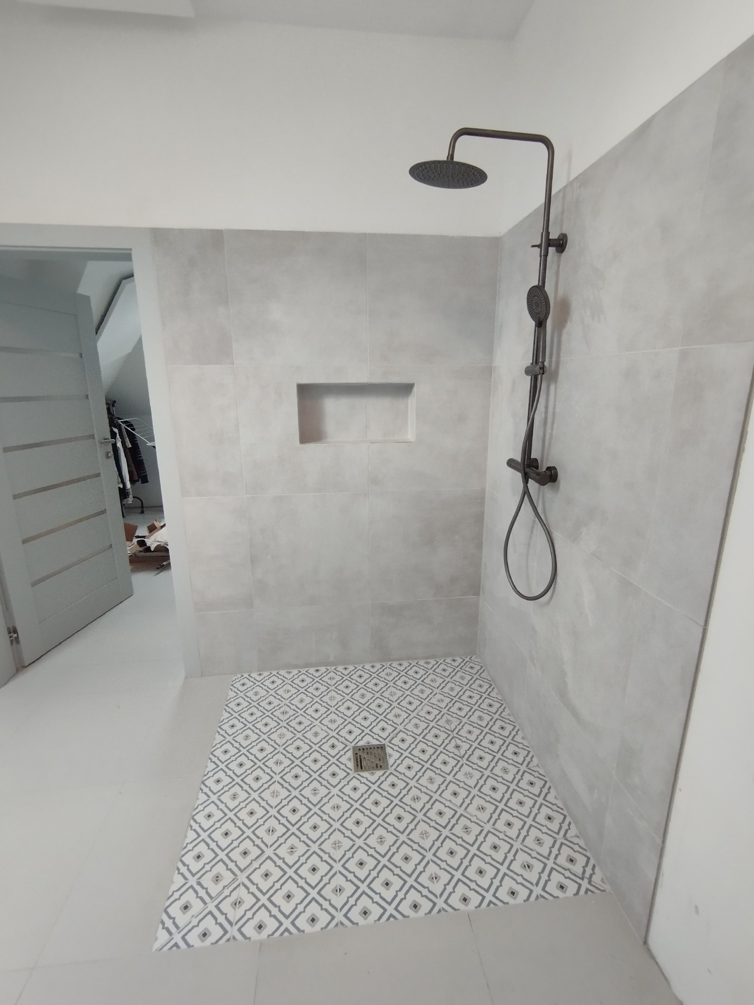 Wykończona kabina prysznicowa z deszczownicą i wzorzystą posadzką w odcieniach szarości, w łazience po remoncie w Białymstoku. W tle widoczne otwarte drzwi.