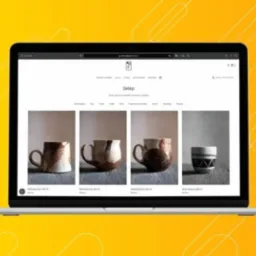 Ekran laptopa prezentujący minimalistyczny design sklepu internetowego z ręcznie robioną ceramiką, widoczne cztery kubki o różnych wzorach i odcieniach brązu, na żółtym tle.