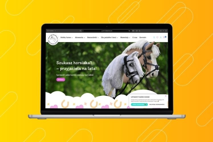 Ekran laptopa wyświetlający stronę internetową z dwoma konikami hobby horse na tle zieleni, z popupem o plikach cookie w prawym dolnym rogu.