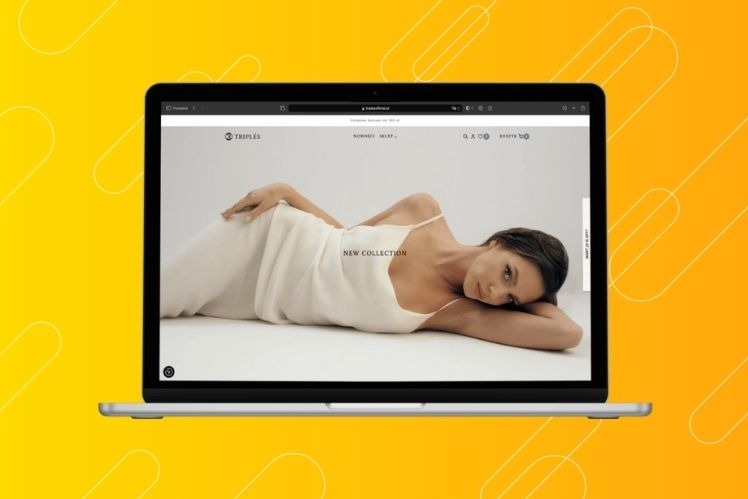 Laptop wyświetla stronę internetową z modelką prezentującą nową kolekcję ubrań na białym tle. Widoczny pasek adresu z nazwą domeny i logo firmy w lewym górnym rogu. Uwagę przykuwa minimalistyczny...
