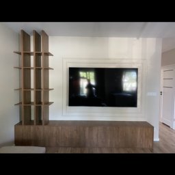 Piotr Kaczmarczyk - Nowoczesna szafka RTV z drewnianymi elementami i pionowym regałem, pod telewizorem w ramie.