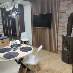 EKOKORBUD Ryszard Kozioł - Jasna jadalnia z okrągłym stołem, białymi krzesłami, kominkiem i telewizorem na ścianie z drewnianych listew.