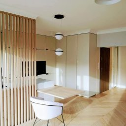 EKOKORBUD Ryszard Kozioł - Jasne wnętrze z drewnianą podłogą w jodełkę, drewnianą ażurową ścianką działową, białym krzesłem i wiszącymi kulistymi lampami, minimalistyczna zabudowa kuchenna w tle.