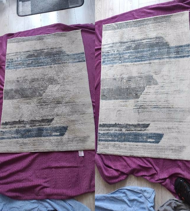 Dwa identyczne dywany z abstrakcyjnym wzorem w odcieniach szarości i błękitu, leżące na fioletowym kocu. Jeden dywan ma widoczną małą białą metkę.