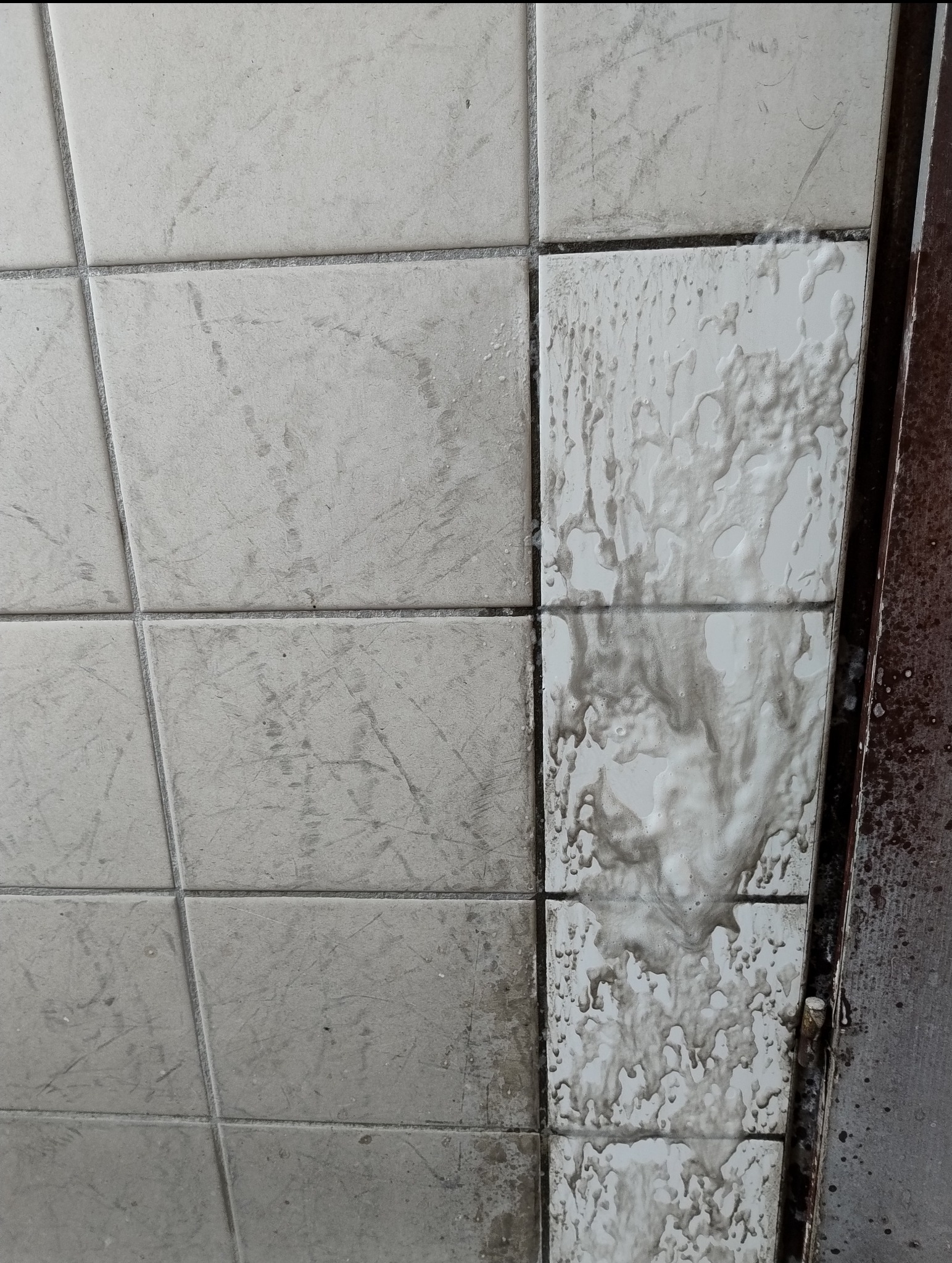 Płytki ścienne częściowo umyte, z widocznym brudem i zaciekami po czyszczeniu, ukazujące efekt przed i po sprzątaniu.