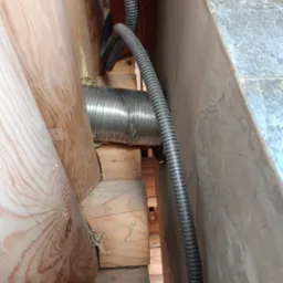 Wnętrze poddasza z widoczną izolacją z wełny mineralnej, rurą wentylacyjną i drewnianą konstrukcją więźby dachowej.