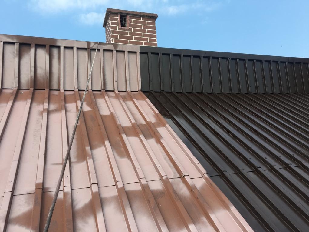 Częściowo pomalowany blaszany dach z ceglanym kominem w tle, ukazujący różnicę koloru przed i po malowaniu.