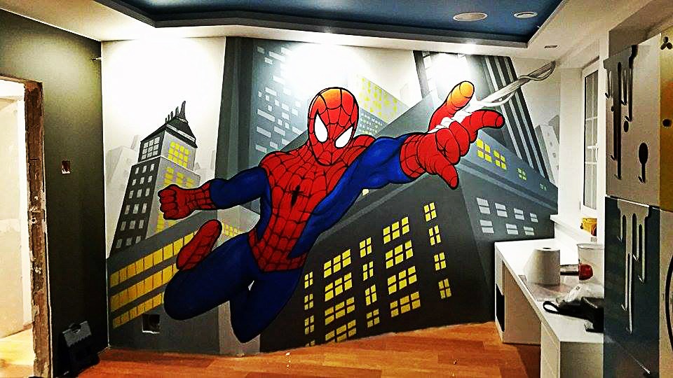 Pokój dziecięcy z ręcznie malowaną ścianą przedstawiającą Spidermana na tle miejskiego krajobrazu, widoczny fragment ściany z niedokończonym wykończeniem i podłoga z paneli.