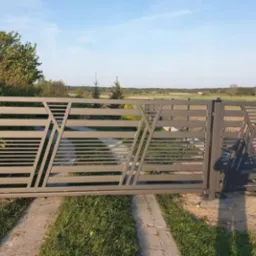 Nowoczesna, przesuwna brama wjazdowa z metalu w kolorze szarym, z poziomymi profilami i ukośnymi wzmocnieniami, na tle zieleni i nieba.