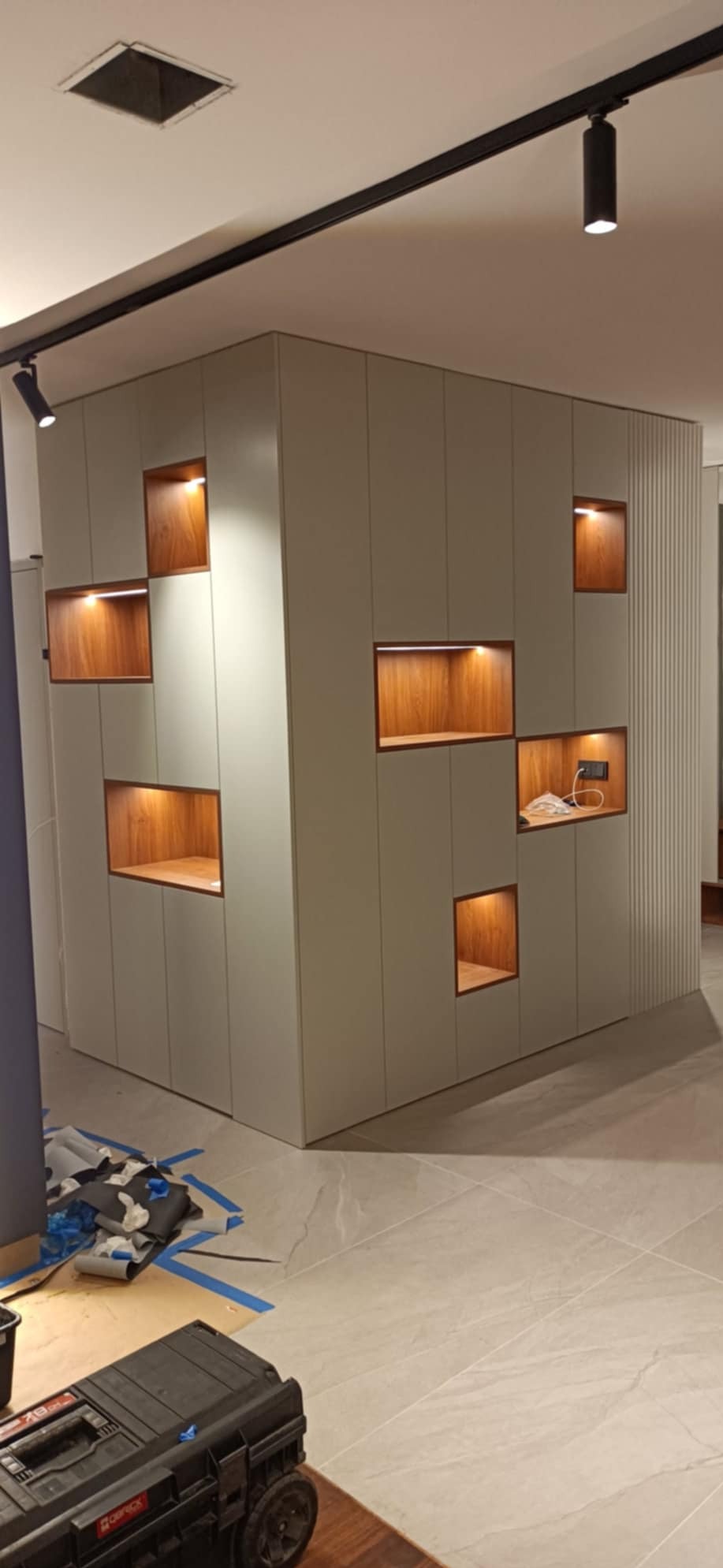 Nowoczesna zabudowa szafy wnękowej z podświetlanymi półkami z drewna w Warszawie, widoczna skrzynka narzędziowa sugeruje prace montażowe.