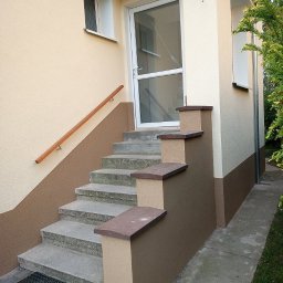 Vitalii Chabaniuk - Dwukolorowa elewacja domu z beżowo-brązowym malowaniem, schody wejściowe z szarego betonu, białe drzwi wejściowe z szybą i drewniana poręcz