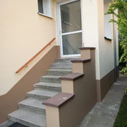 Dwukolorowa elewacja domu z beżowo-brązowym malowaniem, schody wejściowe z szarego betonu, białe drzwi wejściowe z szybą i drewniana poręcz