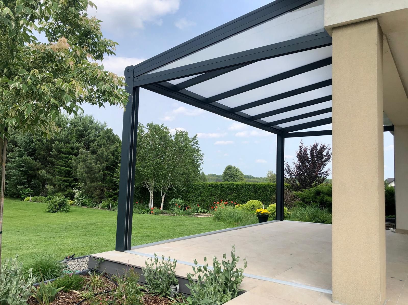 Nowoczesna pergola metalowa z białym zadaszeniem, widok z tarasu na zadbany ogród z zielonym trawnikiem i drzewami. Minimalistyczny design, jasne kolory, słoneczny dzień.