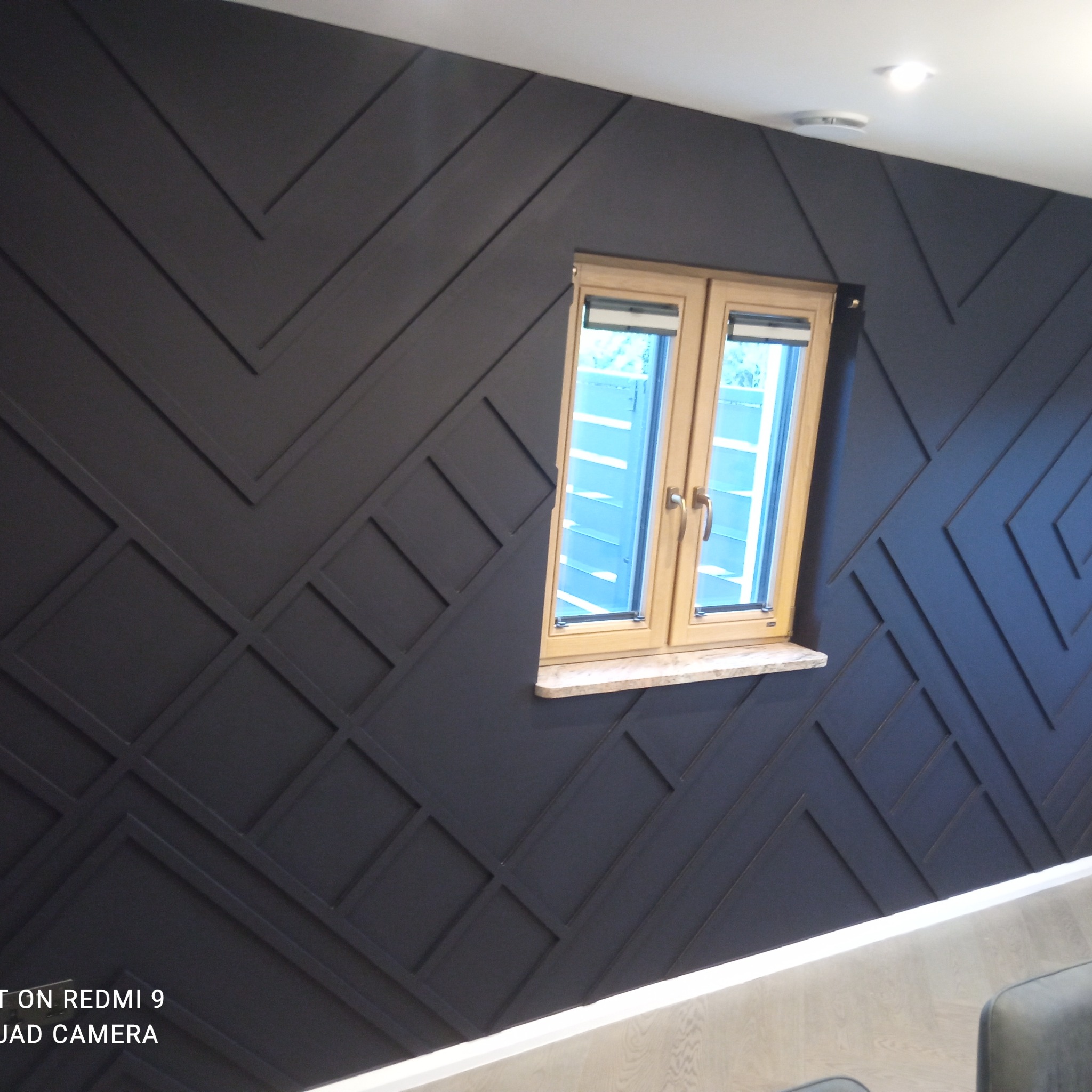 Ciemna ściana z geometrycznym wzorem z listew, okno z jasną ramą. Nowoczesny design wnętrza, subtelne oświetlenie, fragment podłogi.