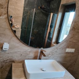 Usługi Ogólnobudowlane Marcin Mąka - Nowoczesna łazienka z umywalką nablatową, baterią w kolorze miedzi i kabiną prysznicową z odpływem liniowym ściennym, widoczna w lustrze. Marmurowe płytki na ścianach i blacie pod umywalką.