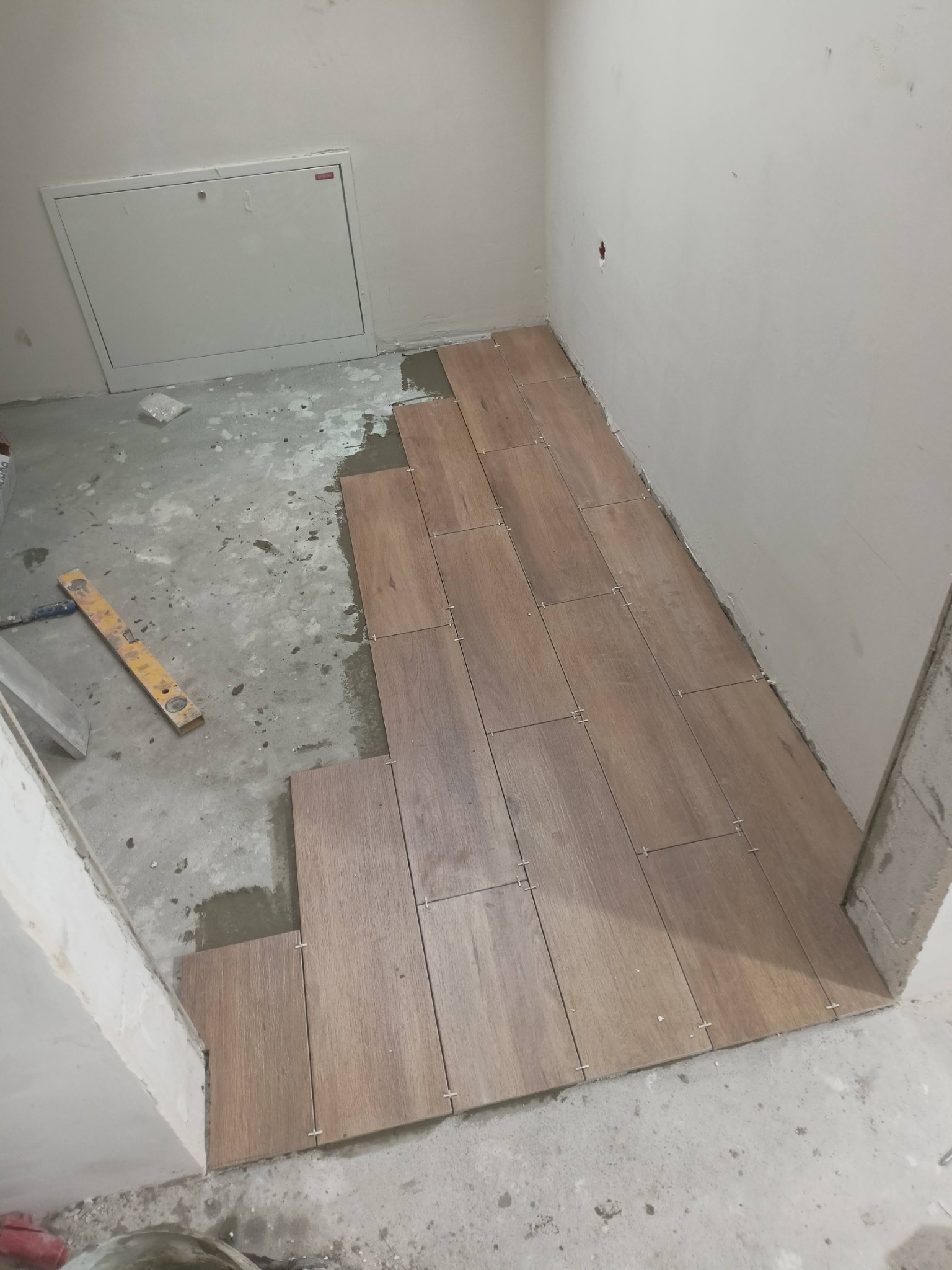 Układanie drewnopodobnych płytek podłogowych w pomieszczeniu w trakcie prac, widoczna poziomica i krzyżyki dystansowe.