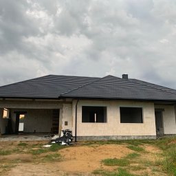 Sztuka Budowania Sp. z o.o. - Surowy budynek z białych pustaków z czarnym dachem z dachówki, widoczny numer domu '23', etap budowy w trakcie prac wykończeniowych, ponure niebo w tle.