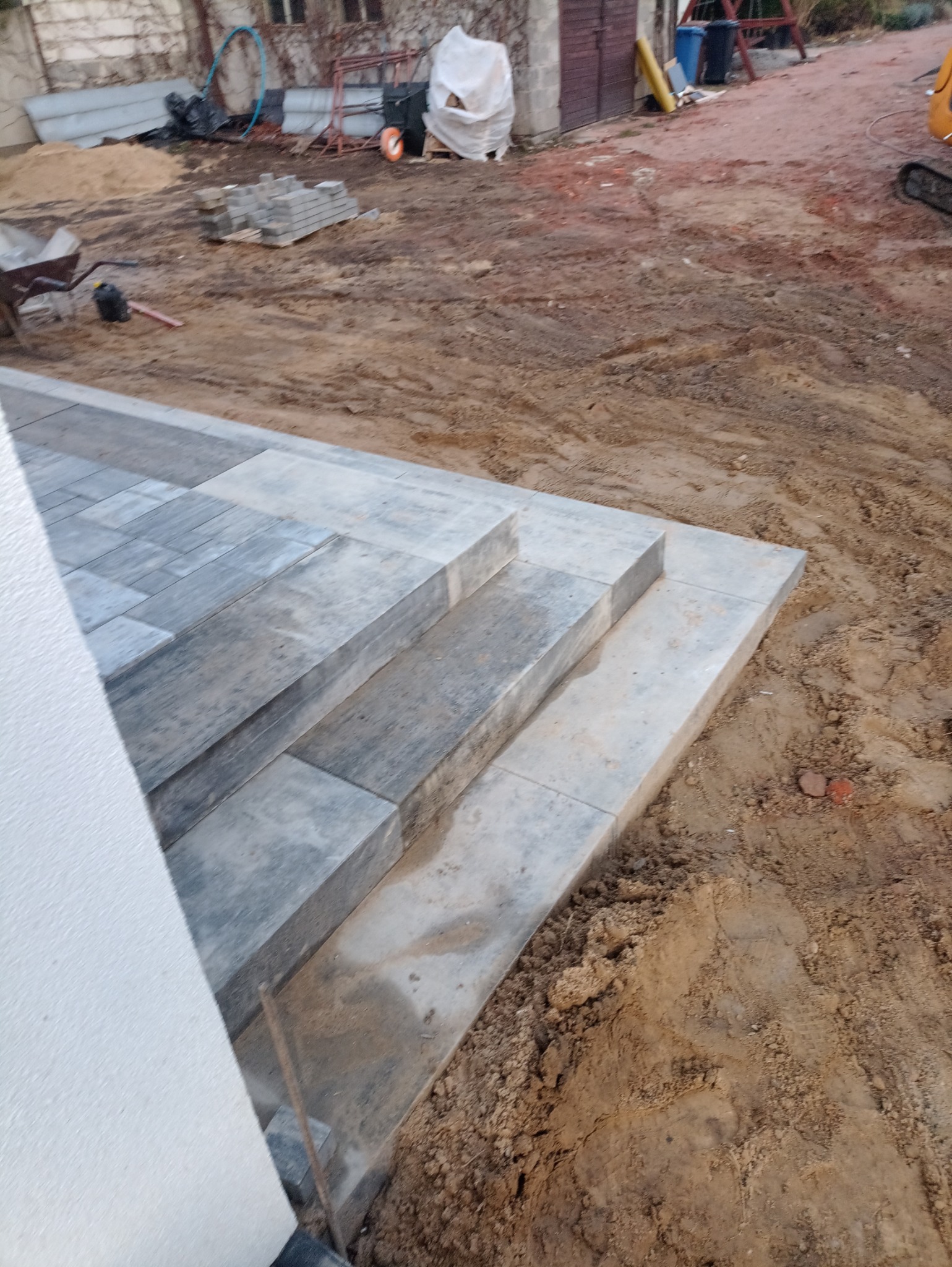 Schody z kostki brukowej w trakcie budowy, widoczne narzędzia i materiały budowlane w tle.