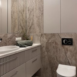 Architekt wnętrz - Małgorzata Juszkiewicz - Elegancka łazienka w neutralnych barwach: umywalka nablatowa, marmurowe płytki, podwieszana toaleta i minimalistyczne szafki. Całość dopełnia tekstylny akcent.