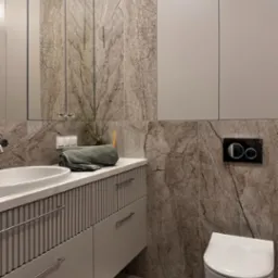 Elegancka łazienka w neutralnych barwach: umywalka nablatowa, marmurowe płytki, podwieszana toaleta i minimalistyczne szafki. Całość dopełnia tekstylny akcent.