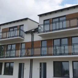 Nowoczesny budynek wielorodzinny z balkonami zabezpieczonymi szklanymi balustradami z czarnymi ramami, widok z dołu na dwa piętra.
