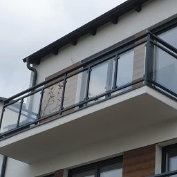 Balu-Inwest - Balkon z czarną ramą i szklanym wypełnieniem, widok z dołu na tle szarego nieba.