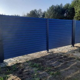 Balu-Inwest - Nowoczesne, poziome ogrodzenie lamelowe w kolorze antracytowym, zlokalizowane w Zbąszyniu, z widoczną siatką ogrodzeniową w tle i niezagospodarowanym terenem u podstawy.