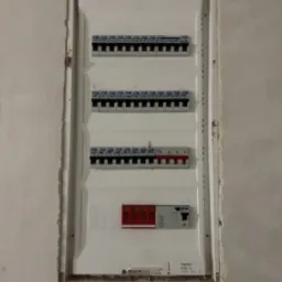 Tablica rozdzielcza z bezpiecznikami i ogranicznikiem przepięć, zamontowana w ścianie w trakcie prac wykończeniowych, widoczne ślady po tynku.