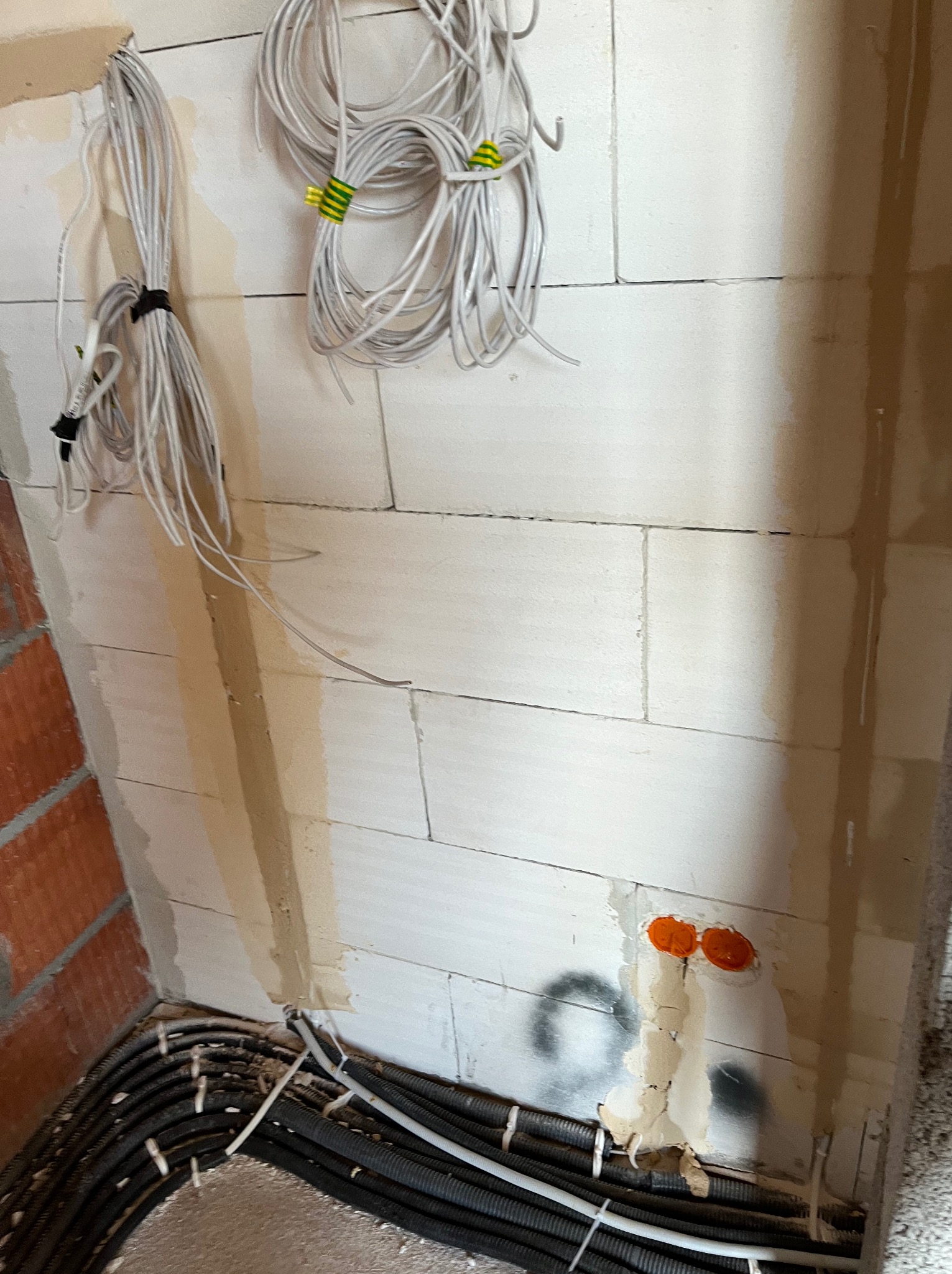 Przewody elektryczne zwisające ze ściany z betonu komórkowego, czarne rury karbowane ułożone w rogu pomieszczenia, pomarańczowe puszki podtynkowe w ścianie.