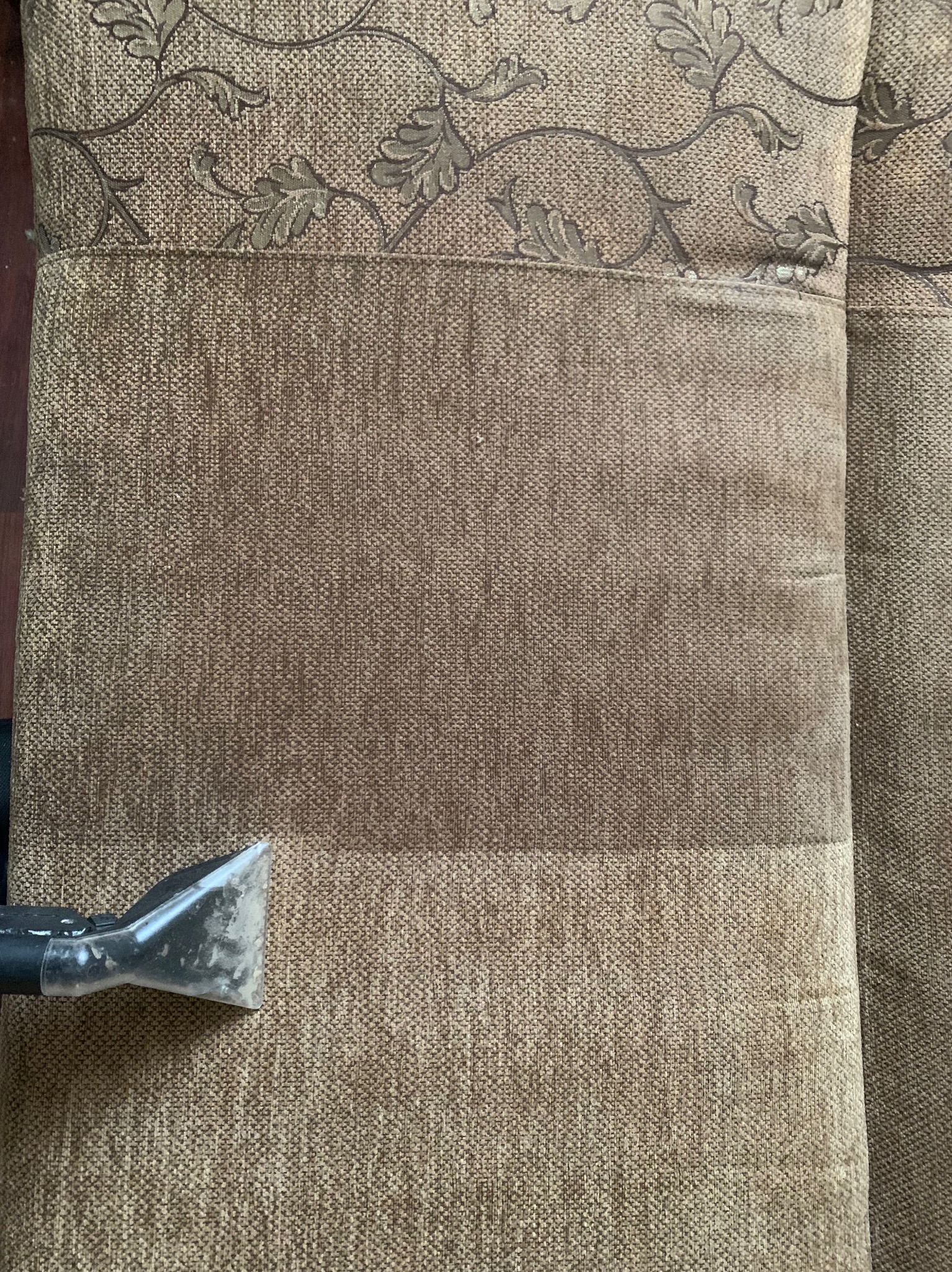 Dysza odkurzacza piorącego na brązowej kanapie z wzorem, widoczna różnica w czystości tkaniny po praniu.