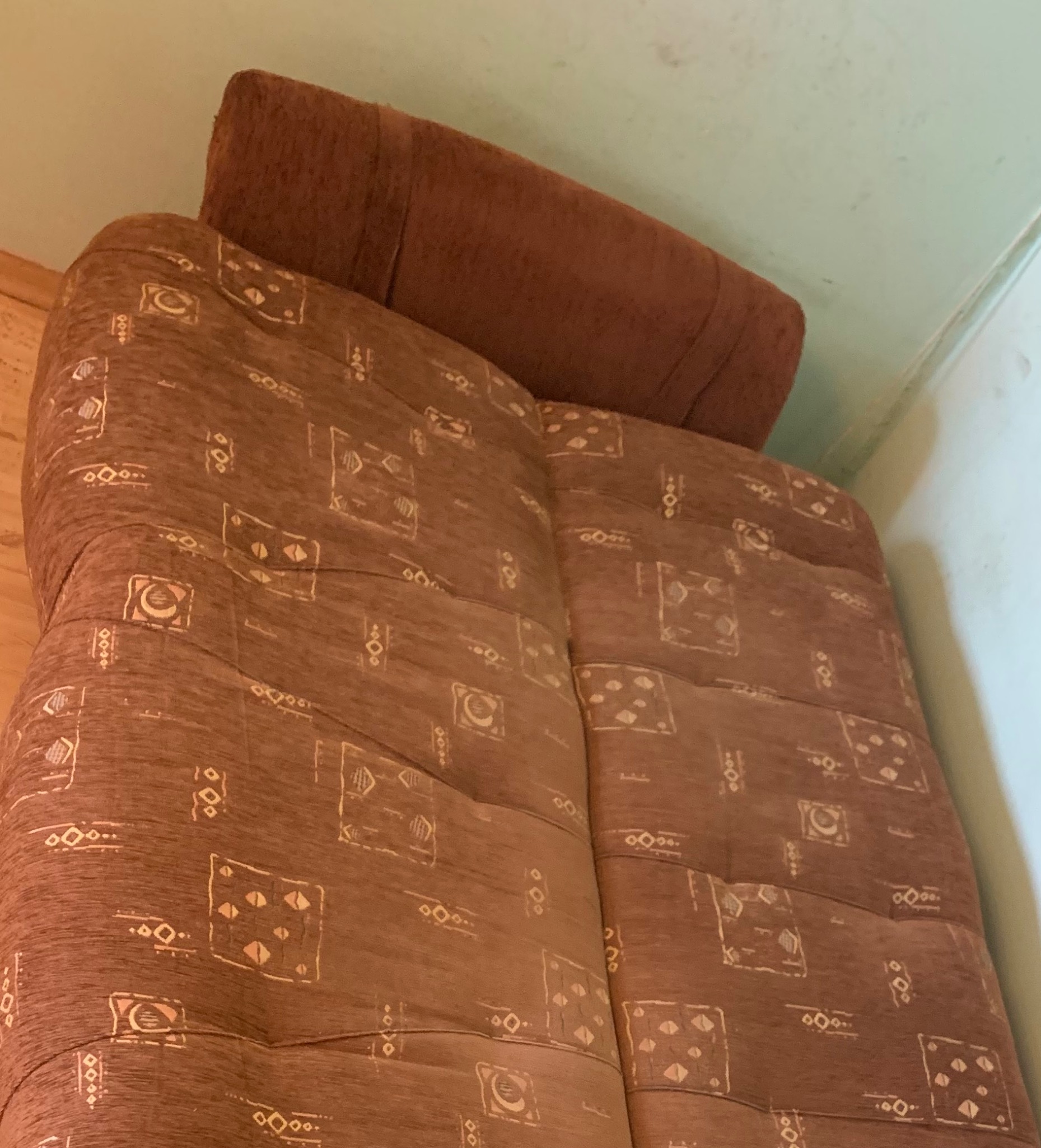 Brązowa kanapa z wzorzystą tapicerką i poduszką w rogu pokoju.