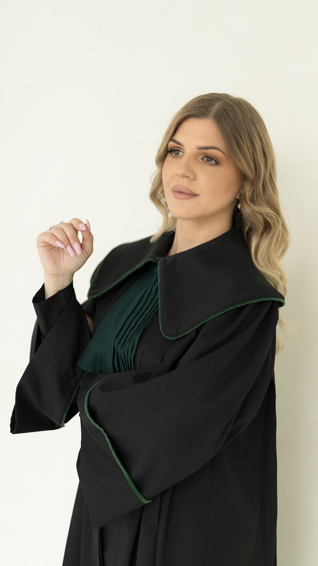 Portret kobiety w todze adwokackiej, z delikatnym uśmiechem i spojrzeniem w bok, na jasnym tle. Widoczne detale togi i subtelny makijaż.