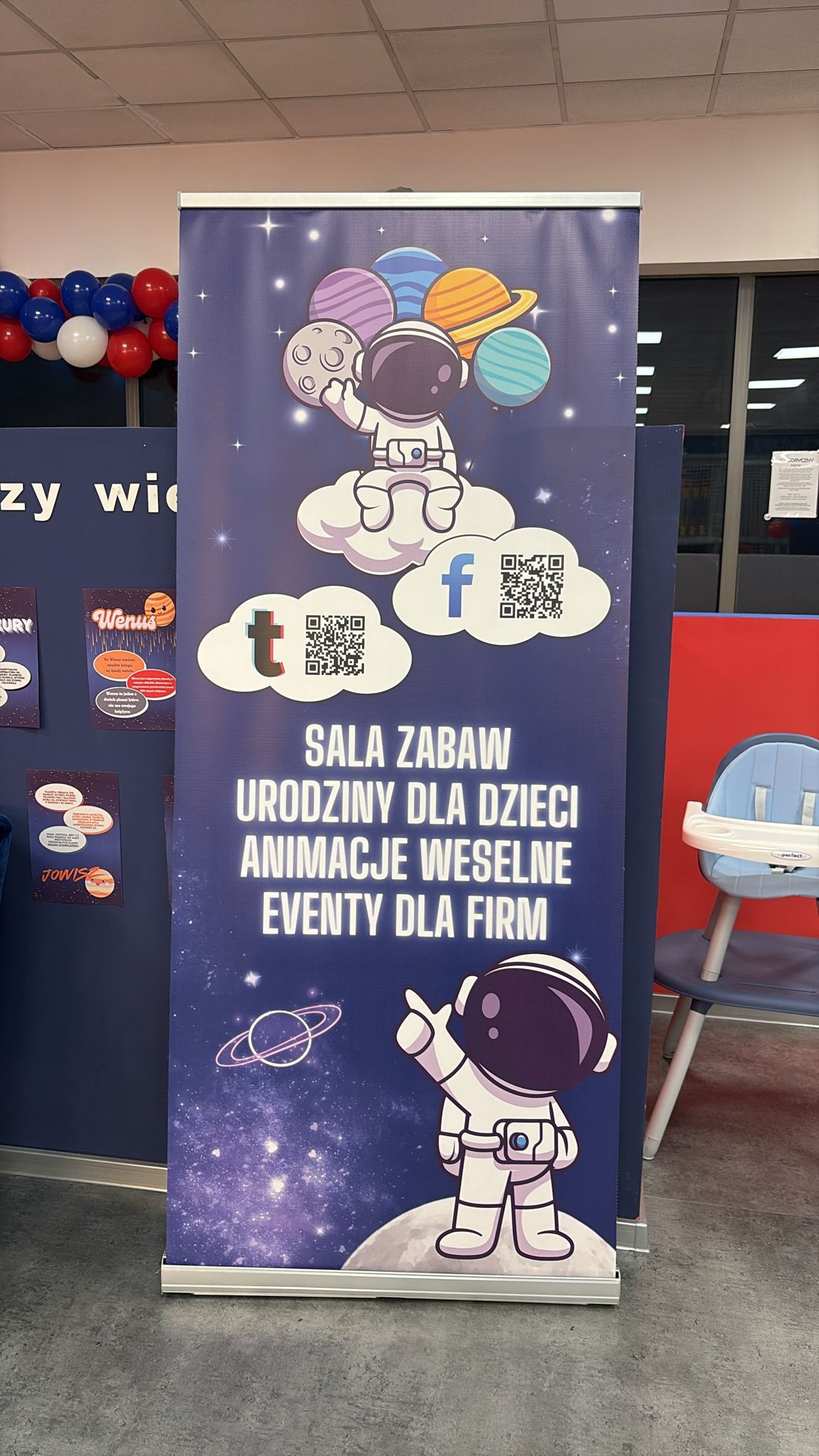 Roll-up reklamowy z motywem kosmosu: astronauci, planety, chmury z kodami QR. Napis: Sala zabaw, Urodziny dla dzieci, Animacje weselne, Eventy dla firm.