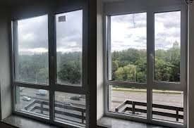 Porównanie okna przed i po umyciu. Po lewej stronie szyba brudna, z zaciekami, po prawej idealnie czysta z widokiem na zieleń drzew i fragment miasta.