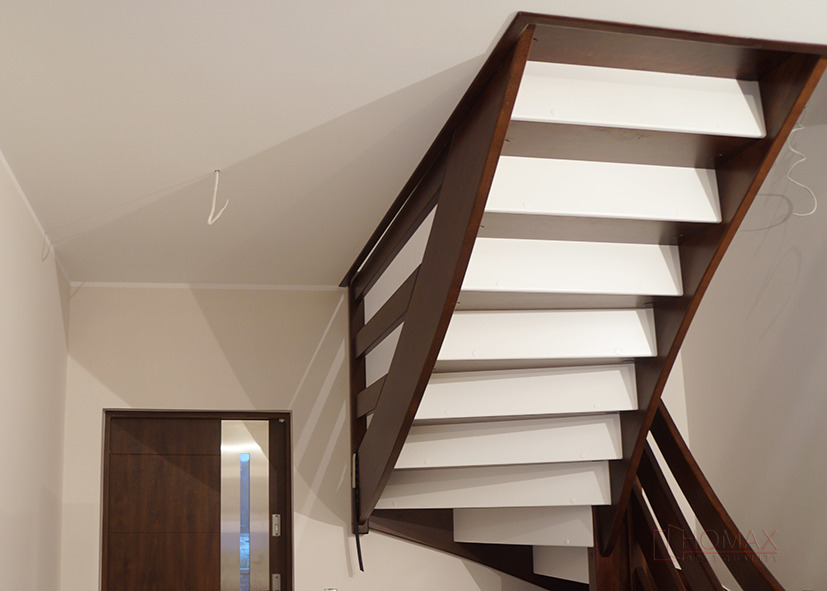 Drewniane schody z białymi stopniami, widziane od dołu, z przesuwnymi drzwiami w tle.