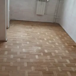 Parkiet ułożony w jodełkę w jasnym pokoju z oknem i grzejnikiem. Świeżo wycyklinowana podłoga z widocznym wzorem drewna.