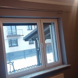 Firma Budowlana Krzysztof Markiewicz - Świeżo pomalowane, gładkie ściany w odcieniach szarości i żółci, widoczne w kadrze z oknem PCV z roletą, przez które widać ośnieżony krajobraz i budynek wielorodzinny z balkonami.