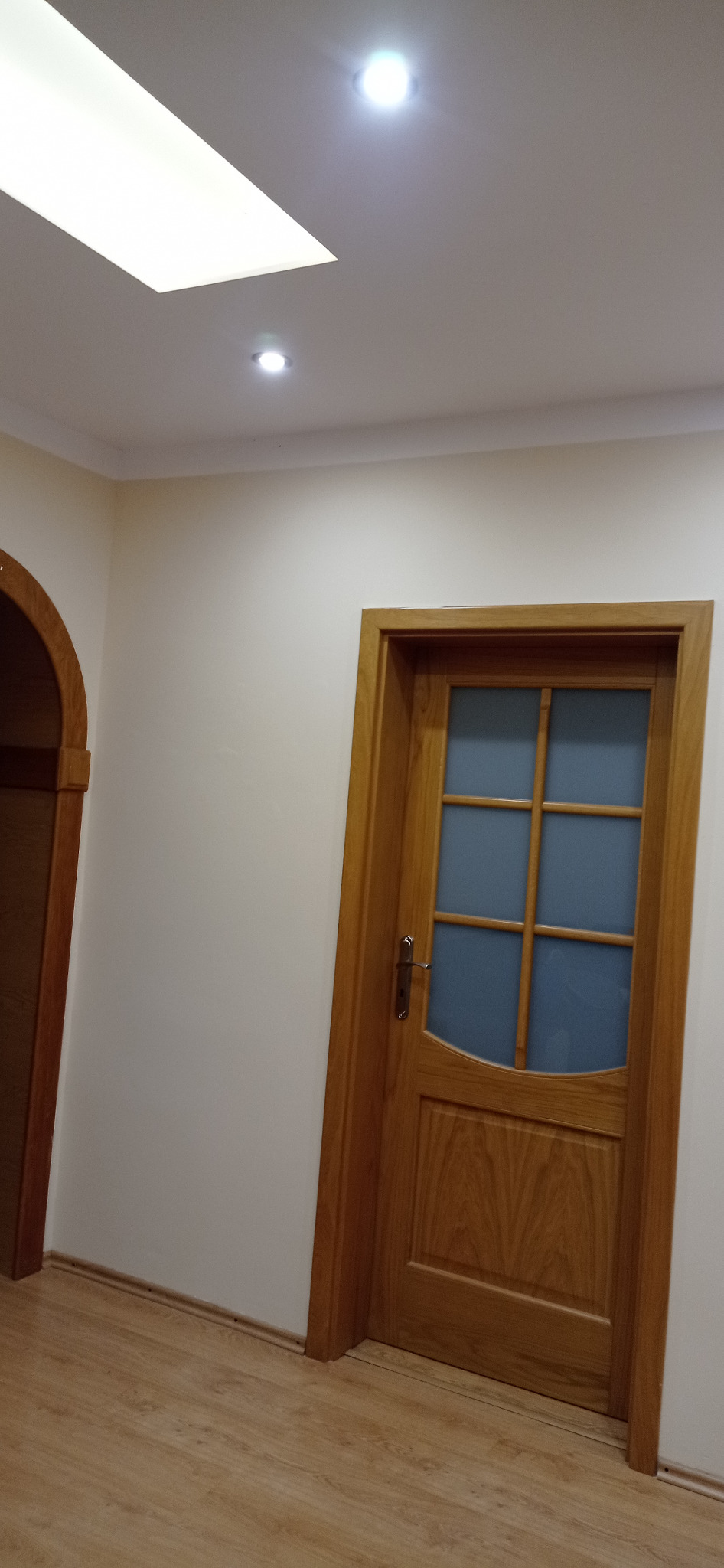 Jasne wnętrze z drewnianą stolarką drzwiową i łukowym przejściem, świeżo po odświeżeniu ścian.