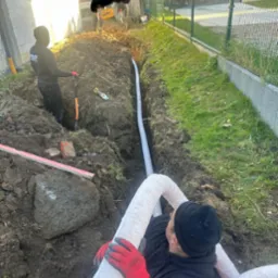 Układanie rur drenażowych w wykopie w Szemudzie, widoczni pracownicy w trakcie montażu systemu.