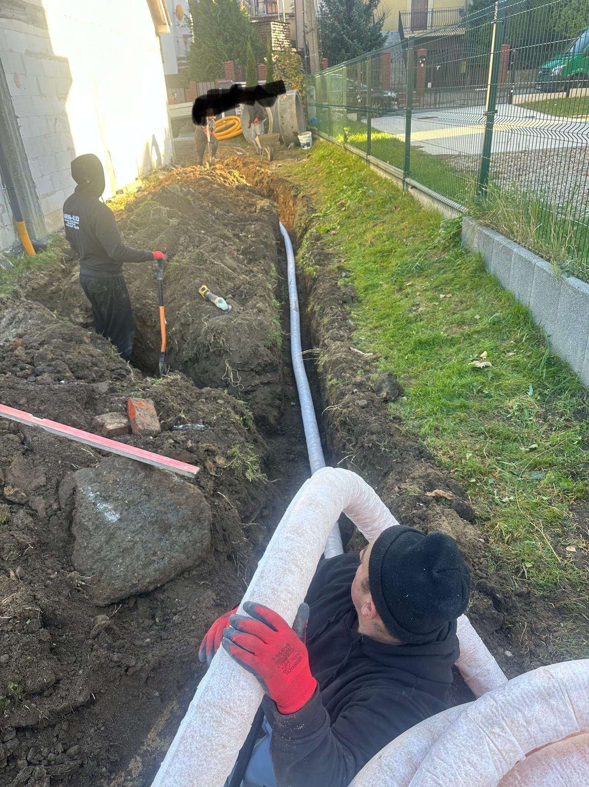 Układanie rur drenażowych w wykopie w Szemudzie, widoczni pracownicy w trakcie montażu systemu.