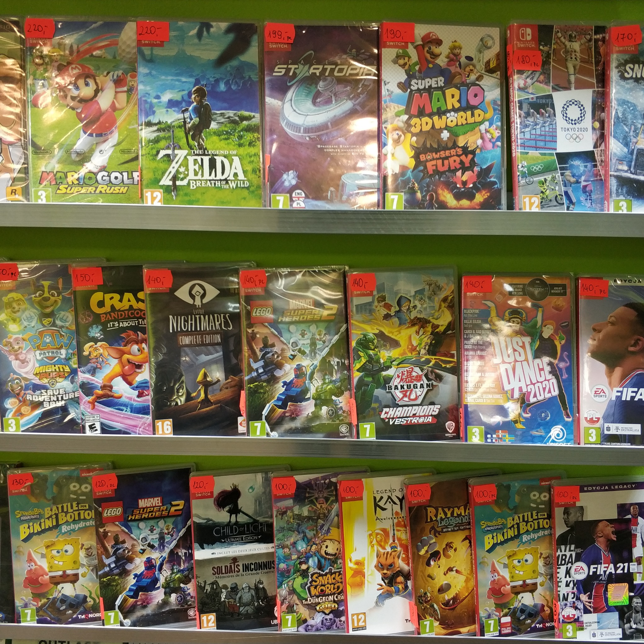 Półka sklepowa wypełniona grami wideo na Nintendo Switch, z widocznymi tytułami takimi jak Mario Golf: Super Rush, Zelda: Breath of the Wild, Super Mario 3D World + Bowser's Fury, FIFA 21 i inne.